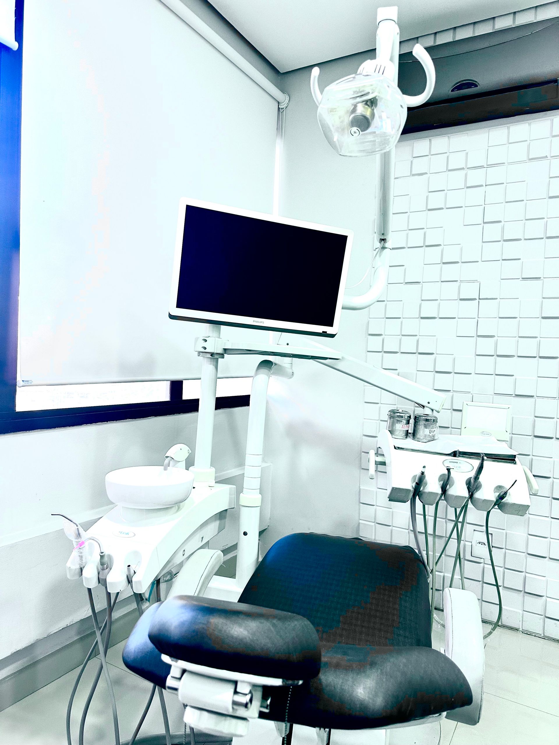 Cadeira odontológica com tela, luz e ferramentas acopladas em um consultório odontológico.
