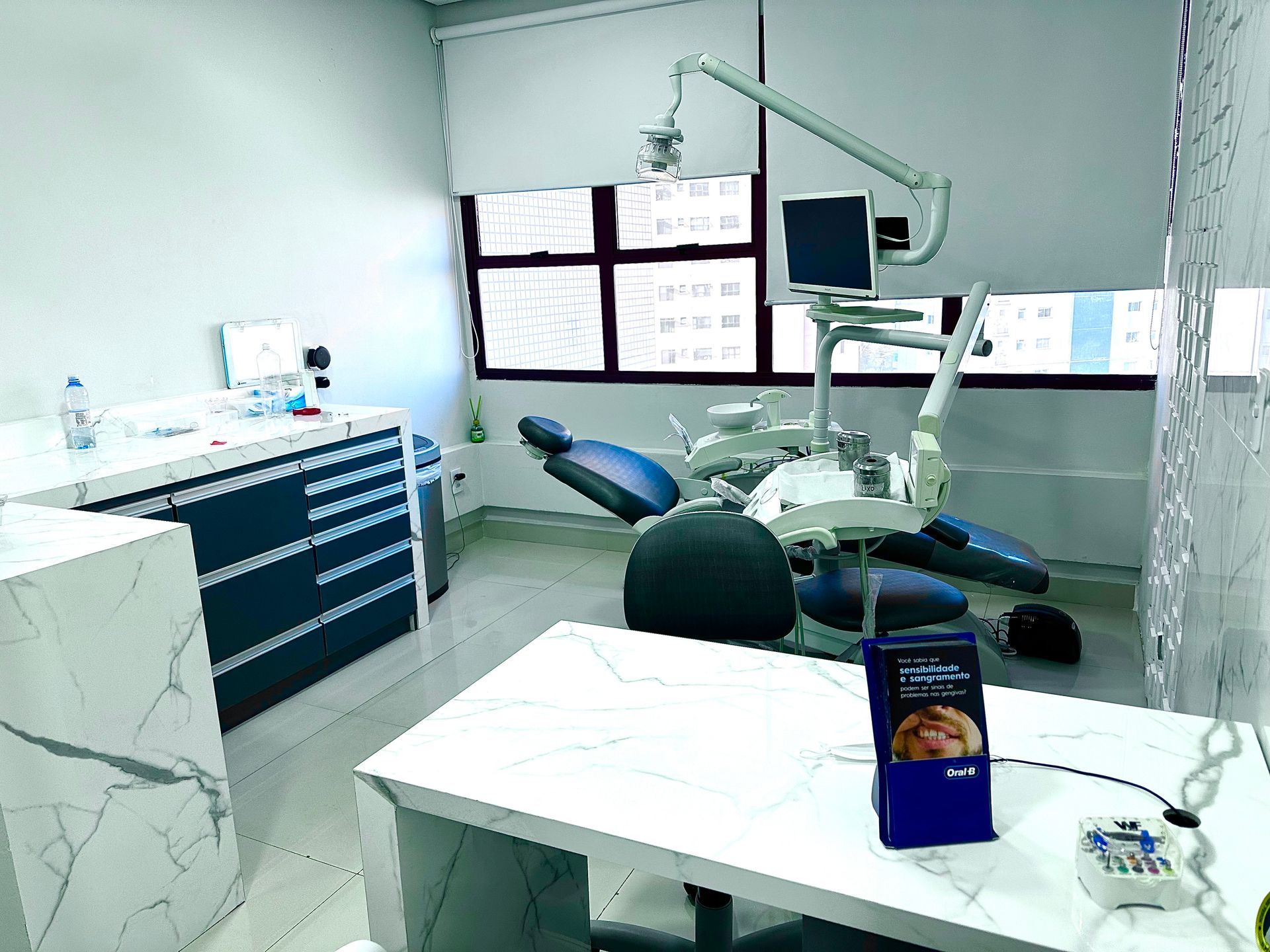 Consultório odontológico com cadeira azul, instrumentos, mesa branca e detalhes em mármore.
