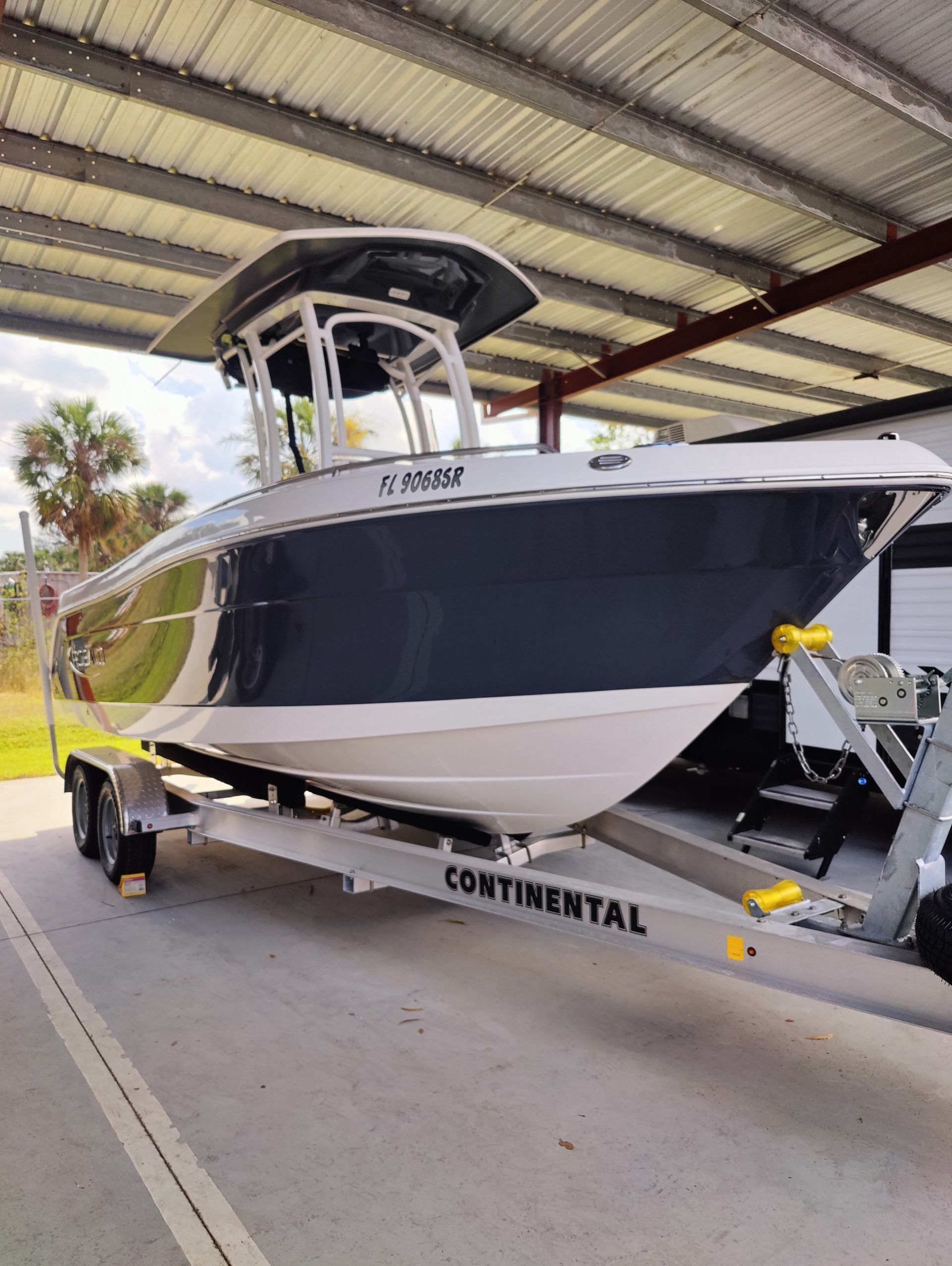 A white and dark blue center console boat on a trailer, under a metal roof.