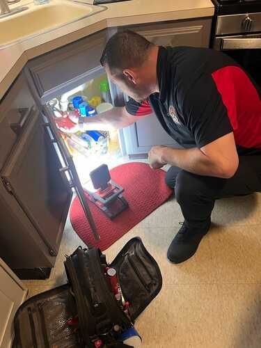 A man is kneeling down in a kitchen looking into a refrigerator.