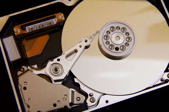 Open hard drive showing a reflective disk, read/write head, and internal components.