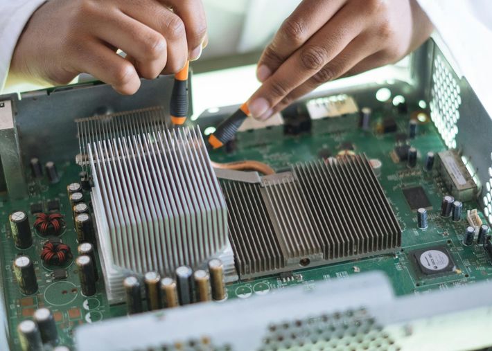 Hands using screwdrivers to repair a circuit board with large heat sinks.