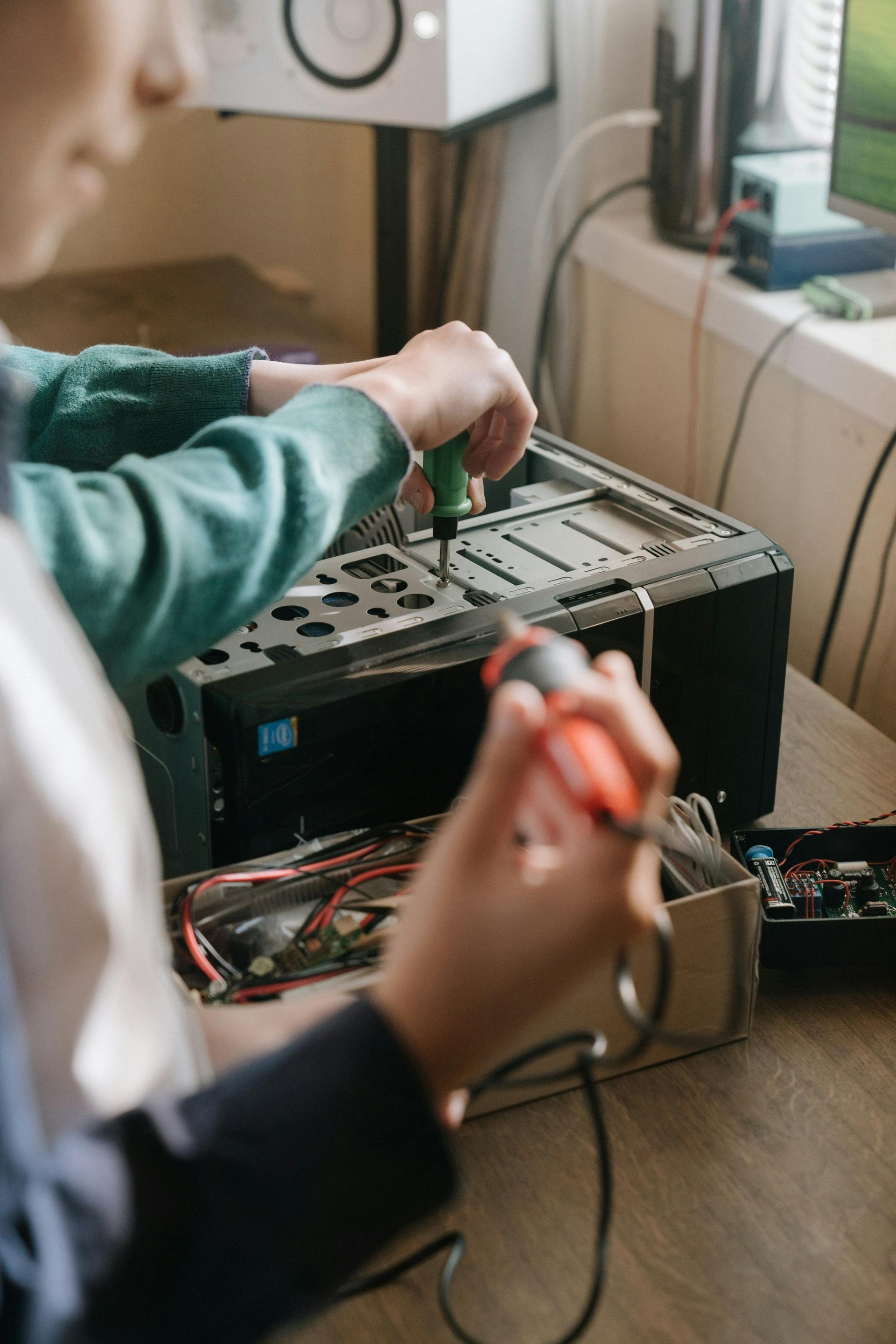 Two people repairing a computer tower, using screwdrivers. Wires and components are visible on a table.