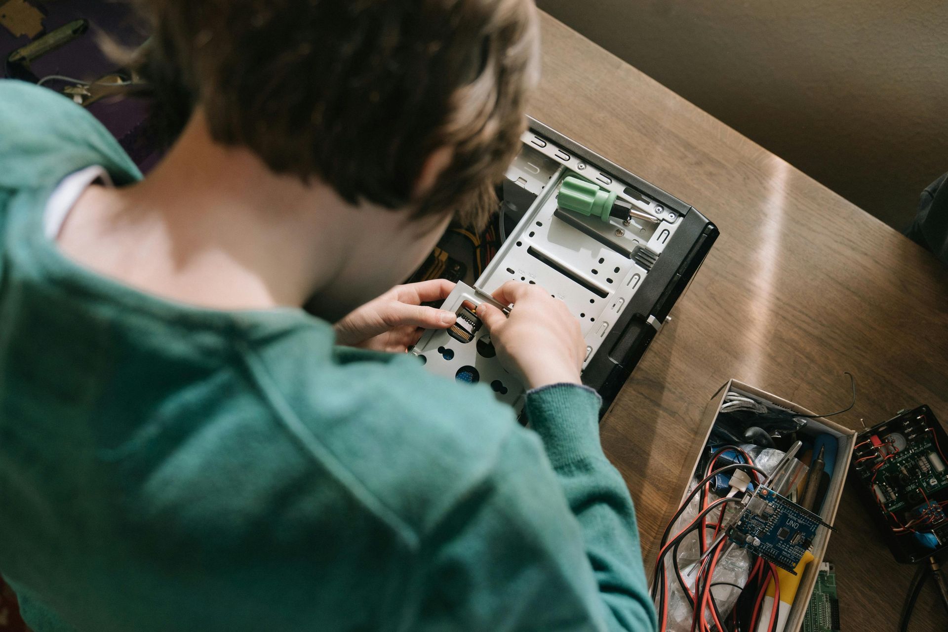 Person in teal sweater working on computer components on a wooden desk.