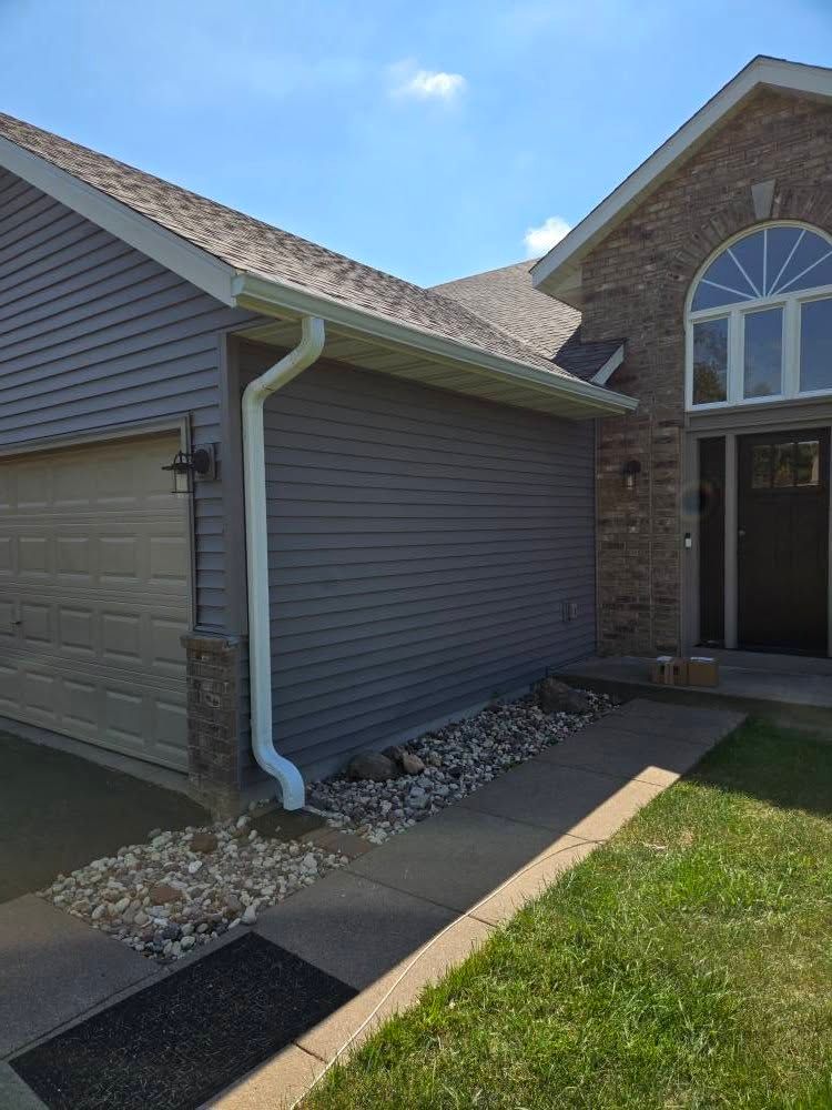 Exterior of a house with gray siding, white gutter, and front entry beside a green lawn