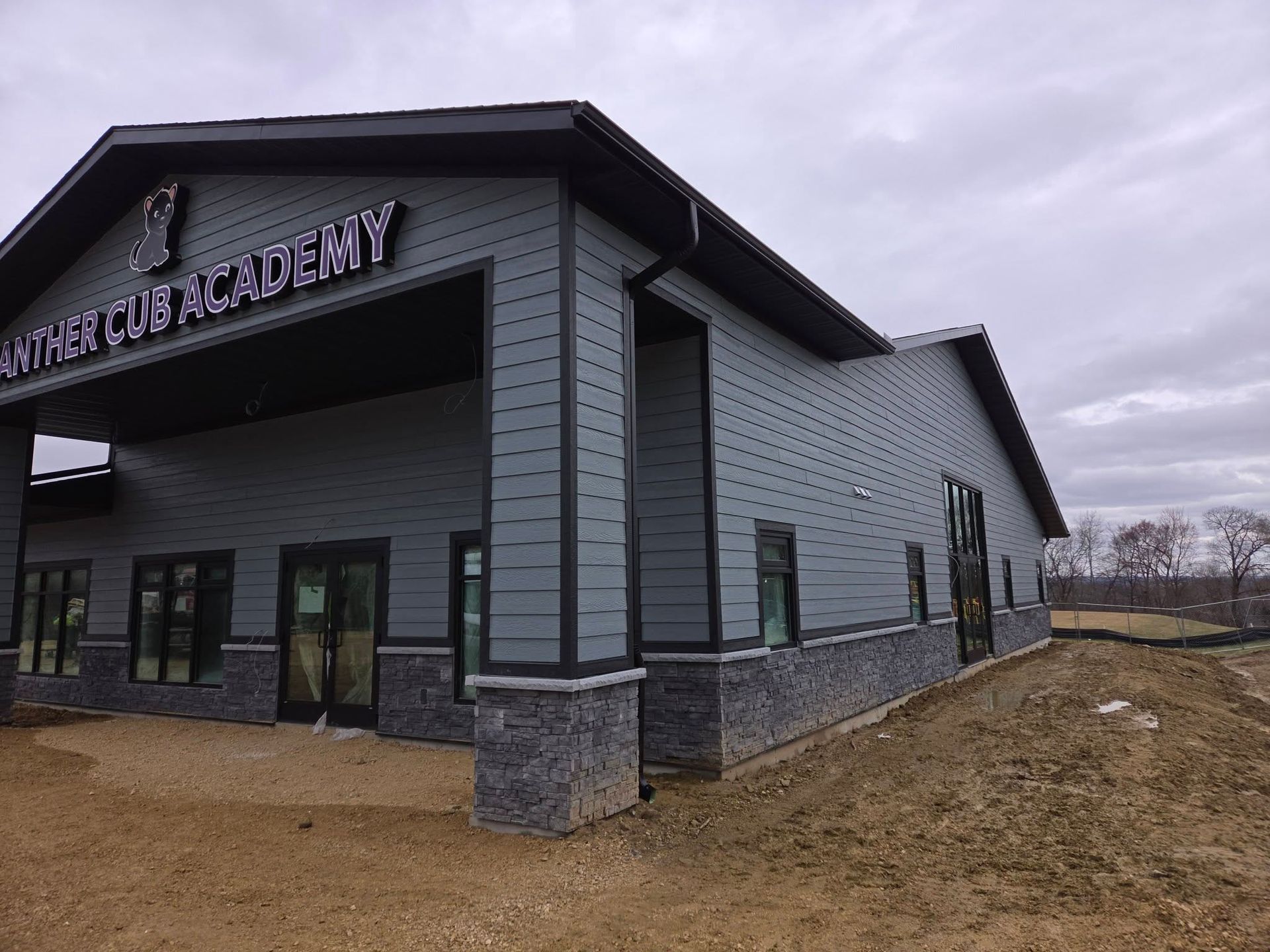 Exterior of a gray Academy building with dark trim under a cloudy sky