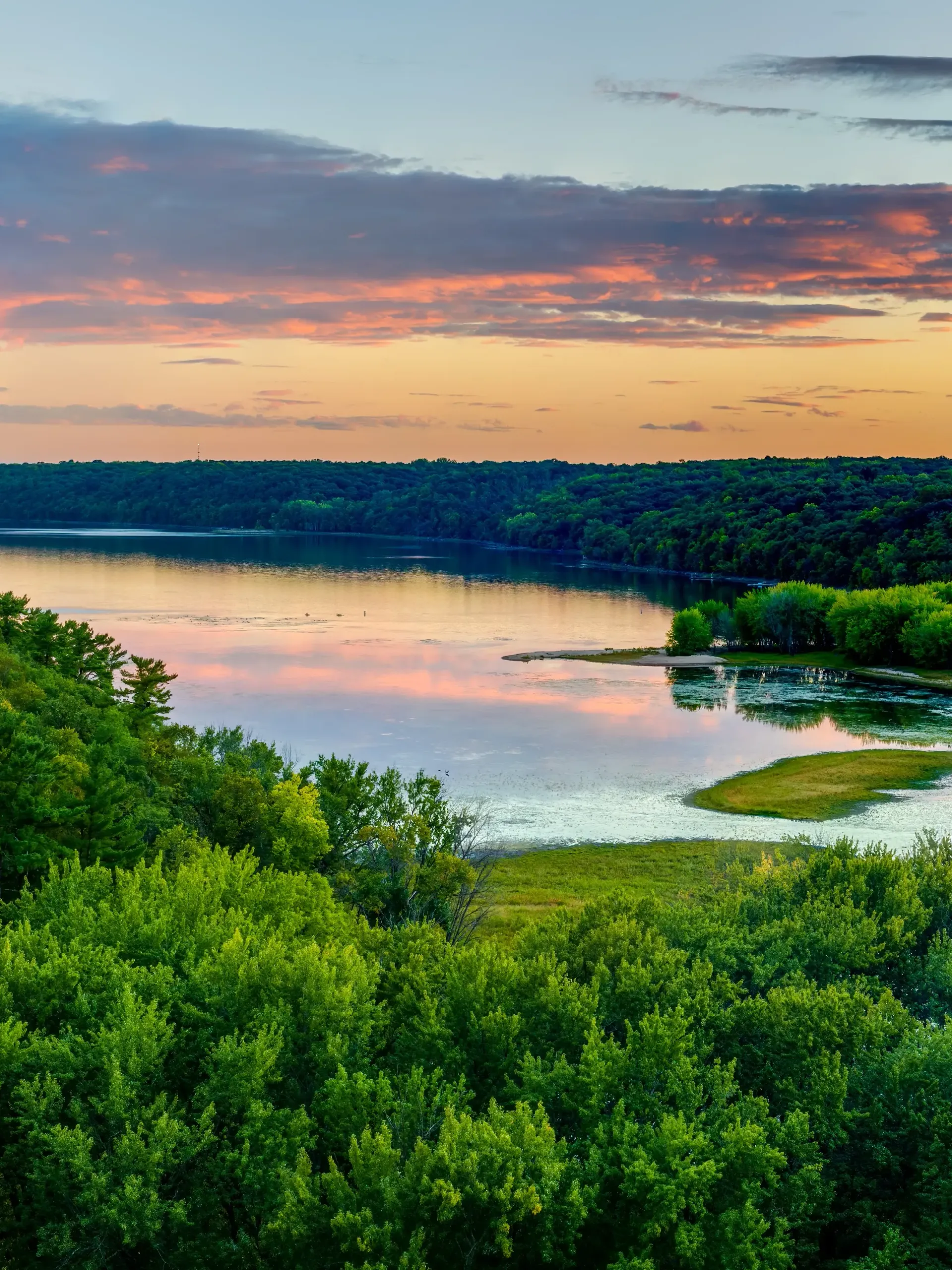 A wooden walkway leading to a gazebo overlooking a body of water at sunset.