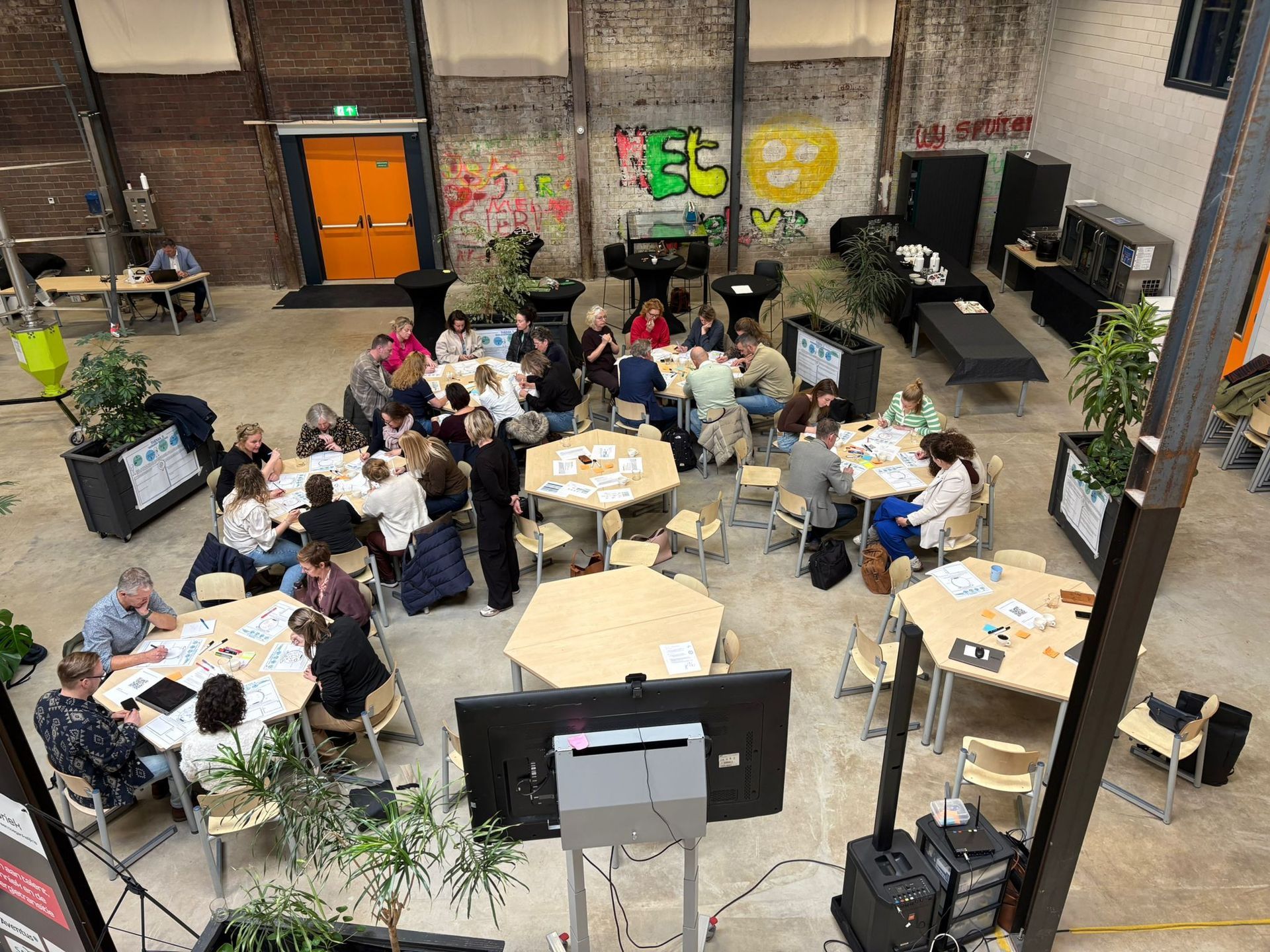 People seated around a table, working. Light-filled room with round table and chairs. Some people are holding objects.
