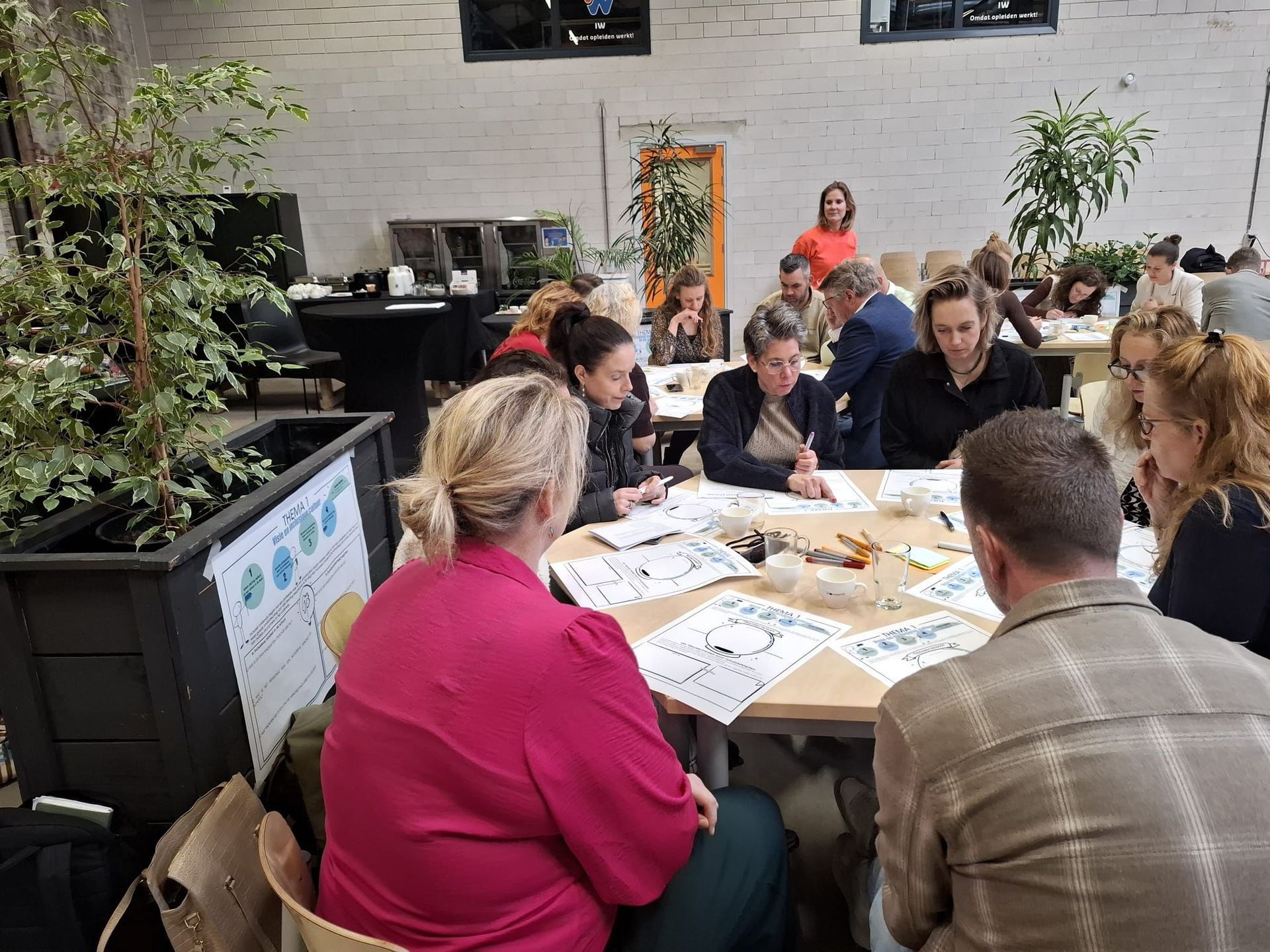 People seated around a table, working. Light-filled room with round table and chairs. Some people are holding objects.