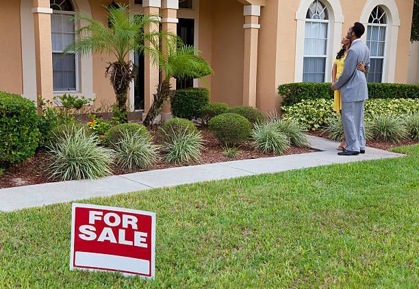 A man and woman are standing in front of a house with a for sale sign in the grass - Perth, WA - Allos Parakletos