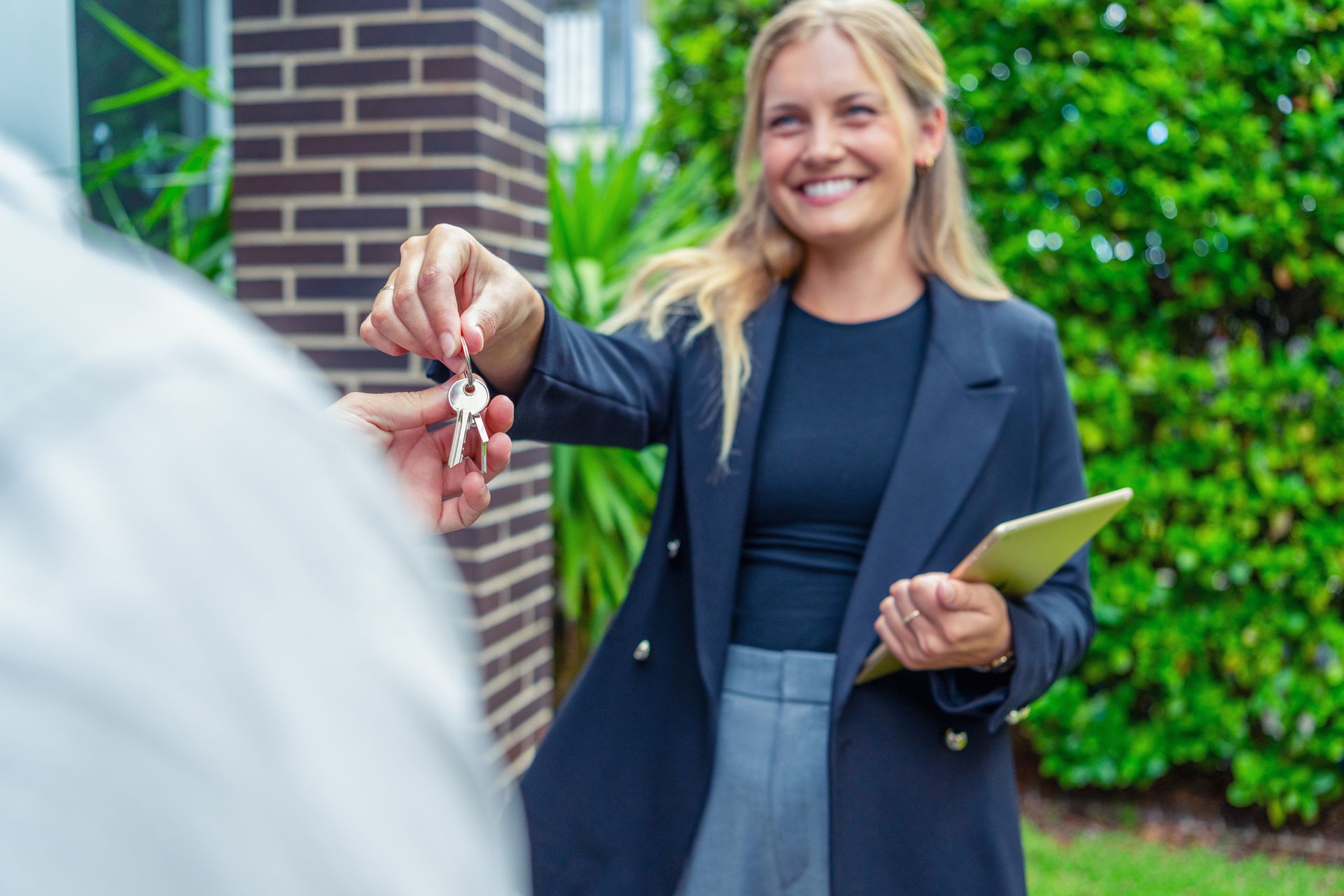 A woman is handing a man a set of keys while holding a tablet - Perth, WA - Allos Parakletos