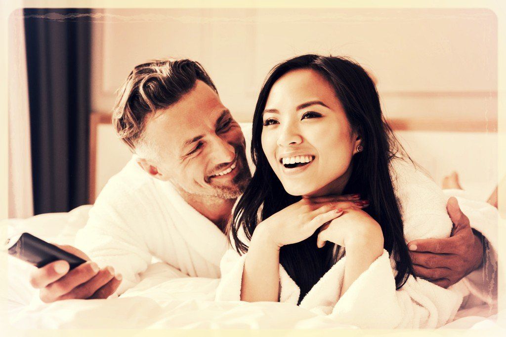 A man and a woman are laying on a bed and smiling