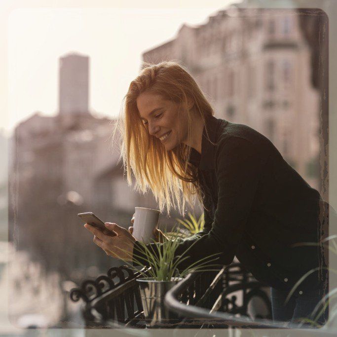 A woman is standing on a balcony looking at her phone.