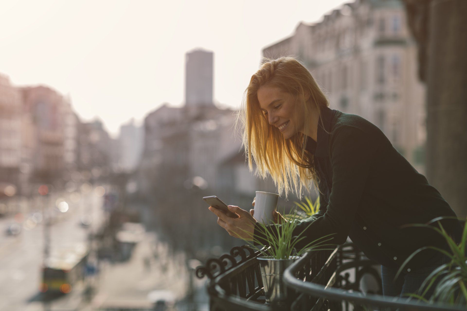 A woman is sitting on a balcony looking at her cell phone.