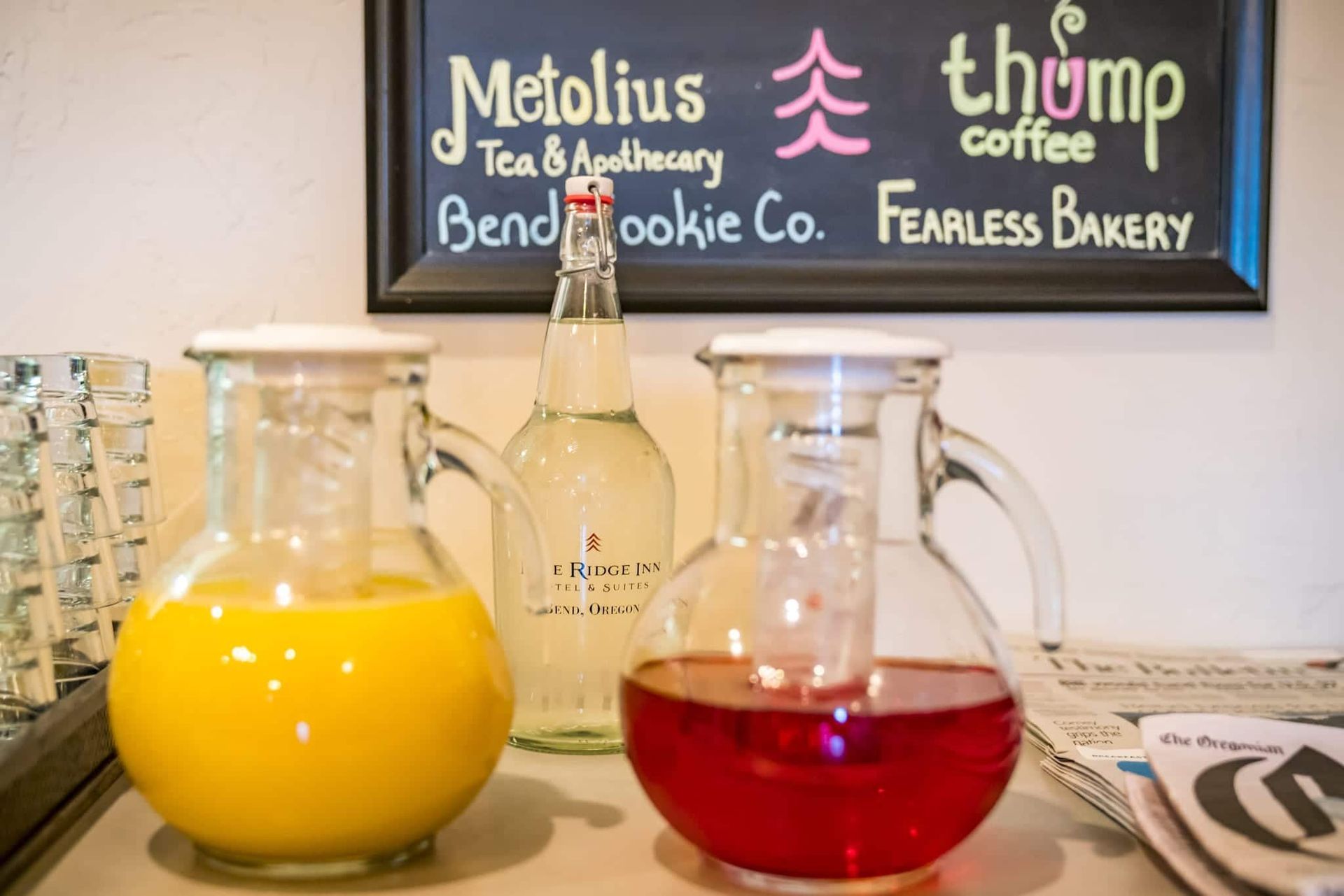Two pitchers of orange juice and a pitcher of red liquid are on a table in front of a sign that says metolius