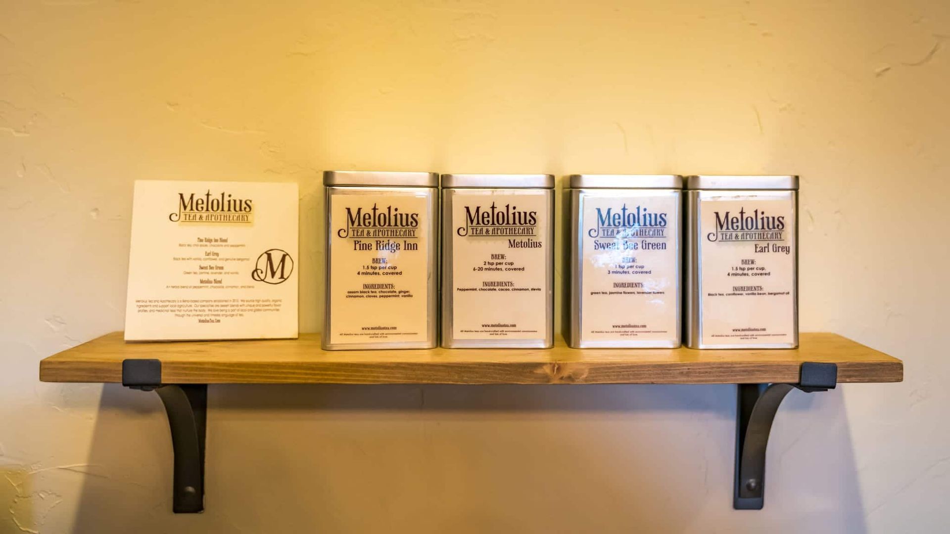 A wooden shelf with four tins of tea on it.