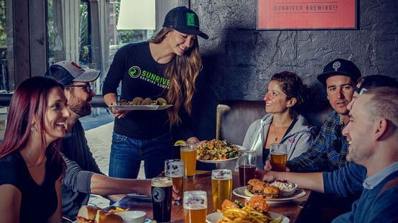 A group of people are sitting at a table in a restaurant eating food and drinking beer.