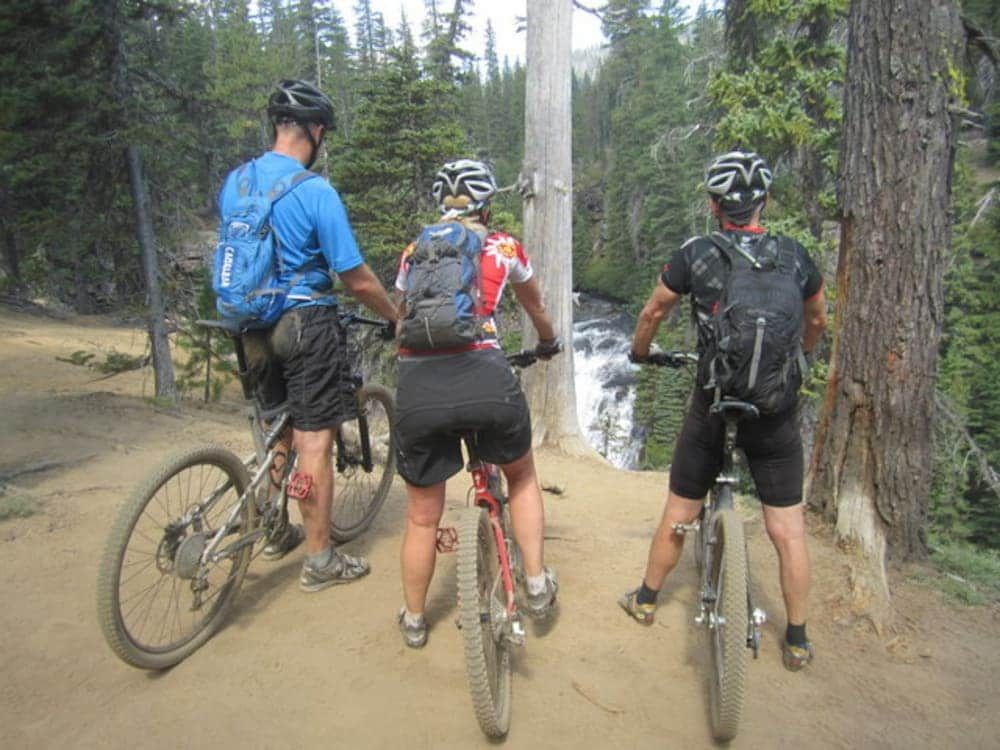 Three people are riding bikes in the woods near a waterfall