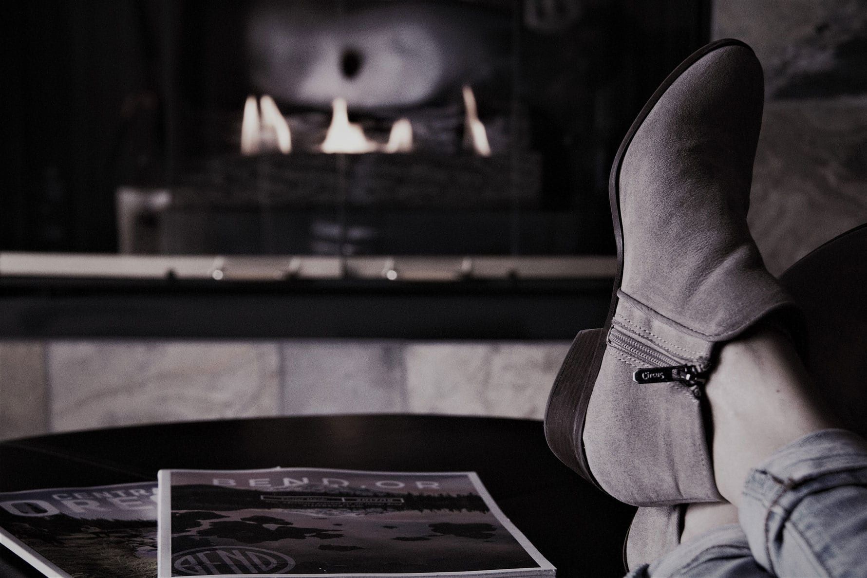 A person is sitting on a couch with their feet up in front of a fireplace.