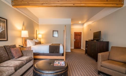 A hotel room with a king size bed , couch , chair , table and television.