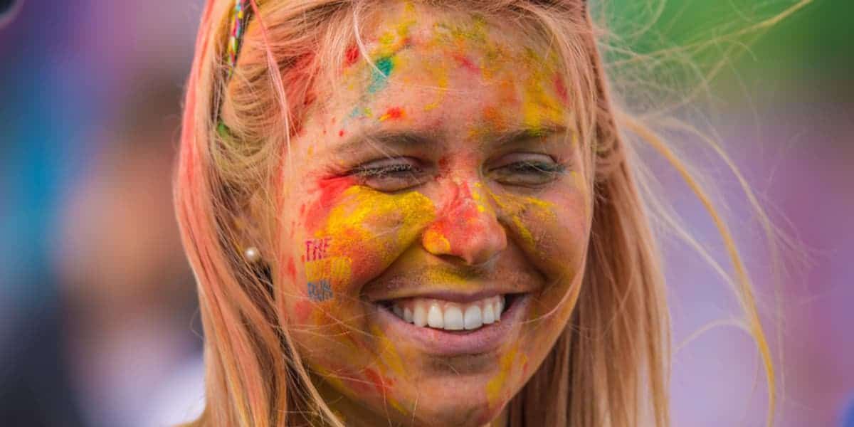 A woman with her face covered in colored powder is smiling.