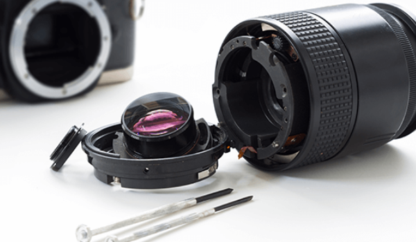 A camera lens is being repaired with a pair of screwdrivers.