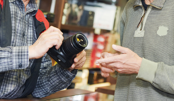 A man is holding a camera and talking to another man in a store.