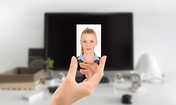 A person is holding a picture of a woman in front of a computer screen.