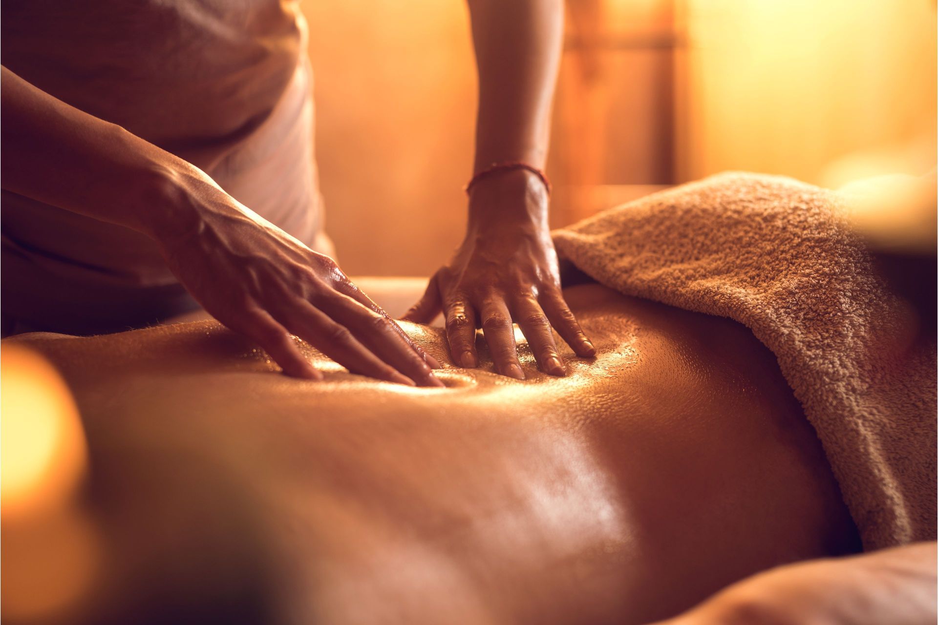 Hands massaging a person's back in a dimly lit setting. A towel is visible.