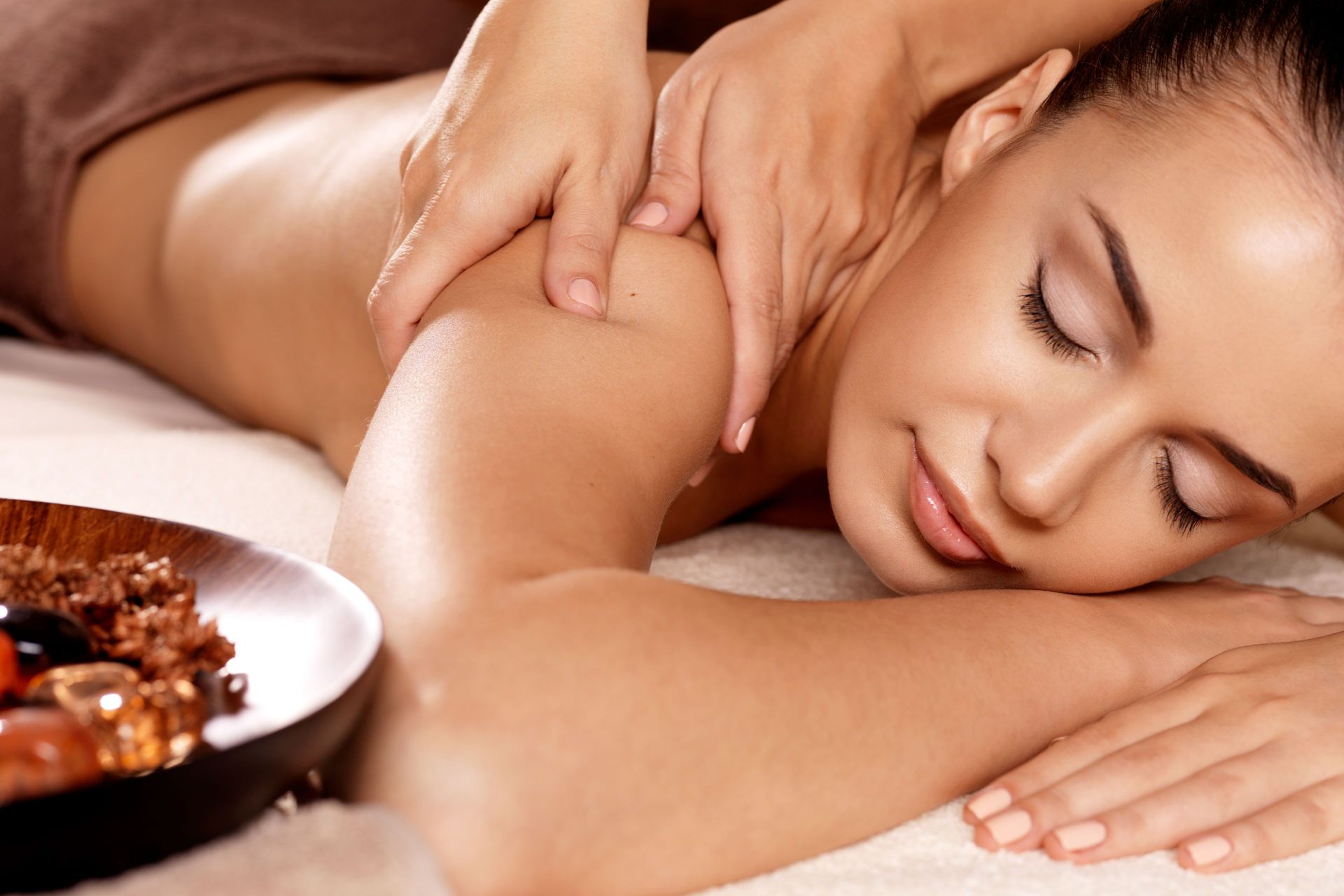 Woman receiving shoulder massage, eyes closed, spa setting.