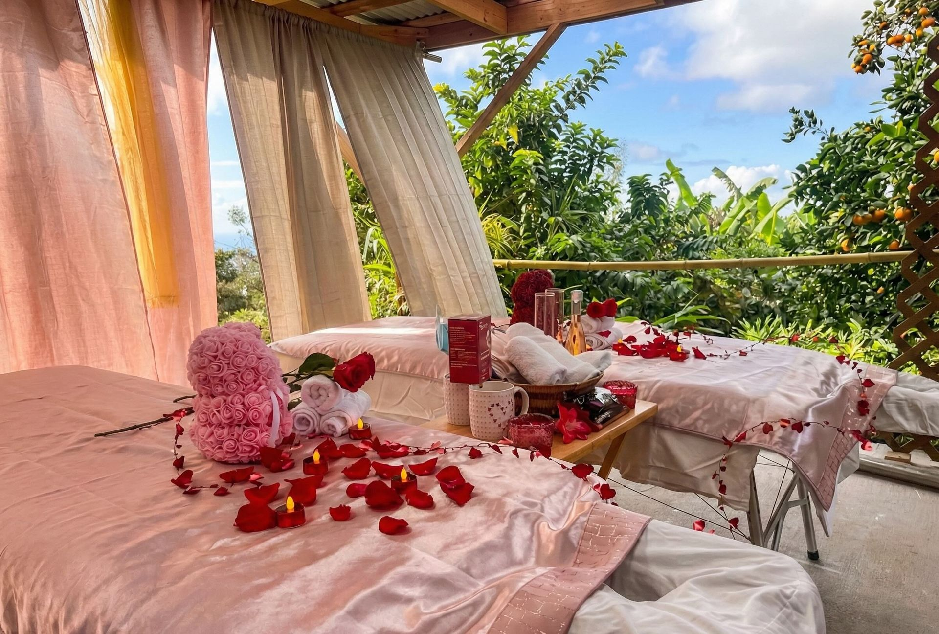 Outdoor massage tables decorated with red rose petals, overlooking a lush green landscape.