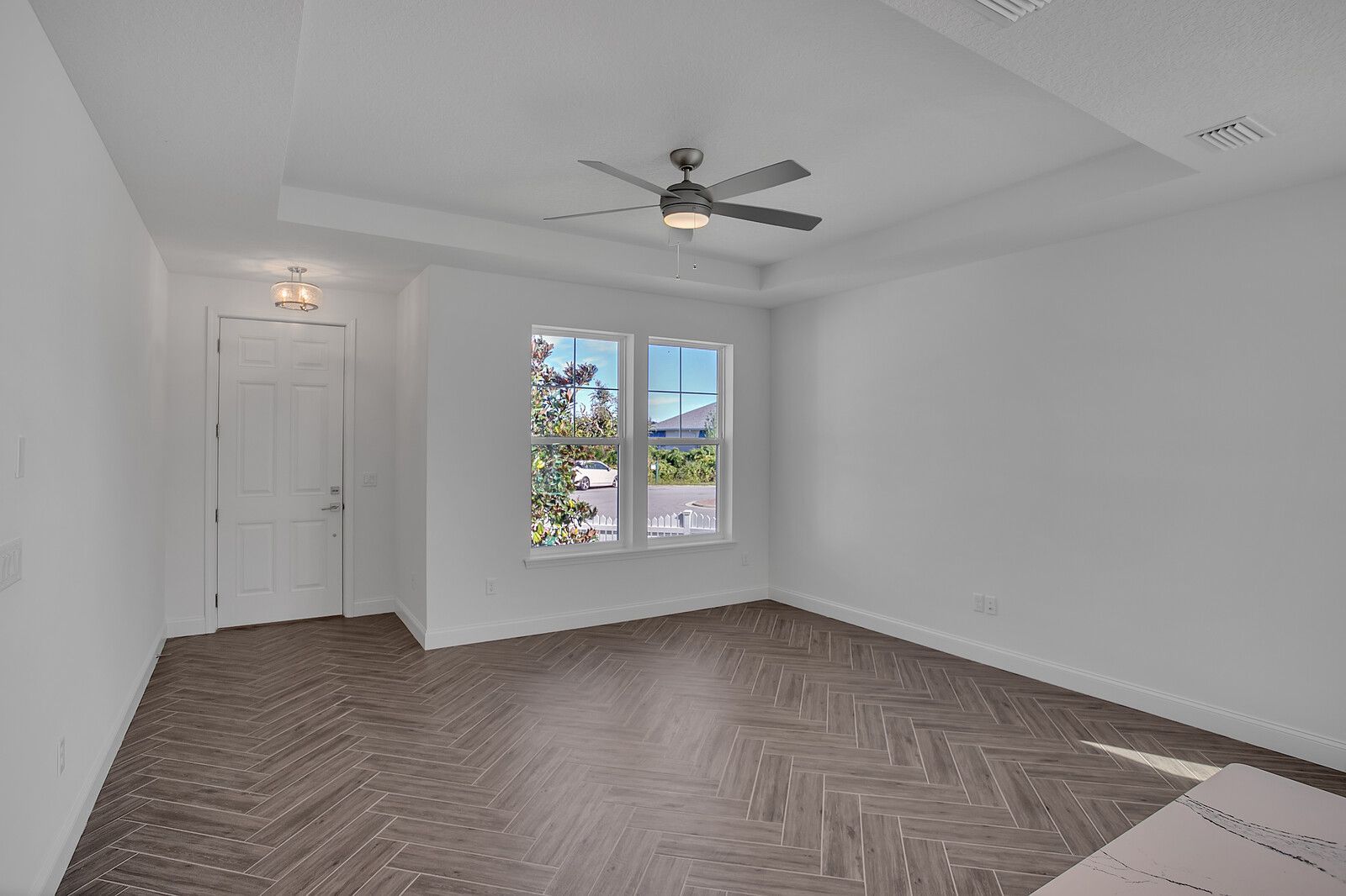 An empty room with a ceiling fan and two windows.