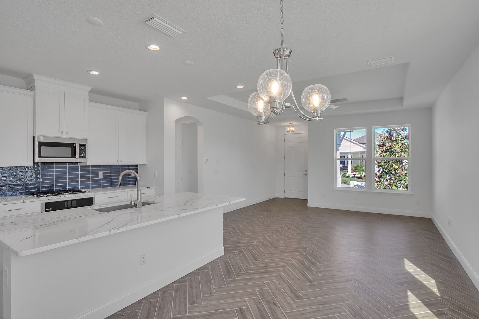 An empty kitchen with white cabinets and a chandelier hanging from the ceiling.