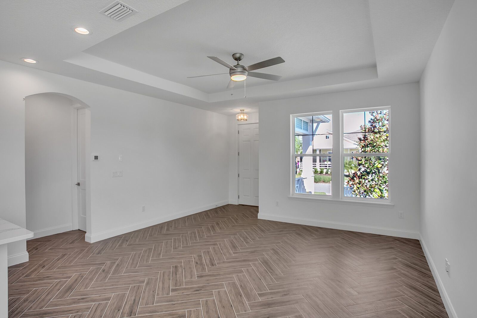 An empty living room with a ceiling fan and two windows.