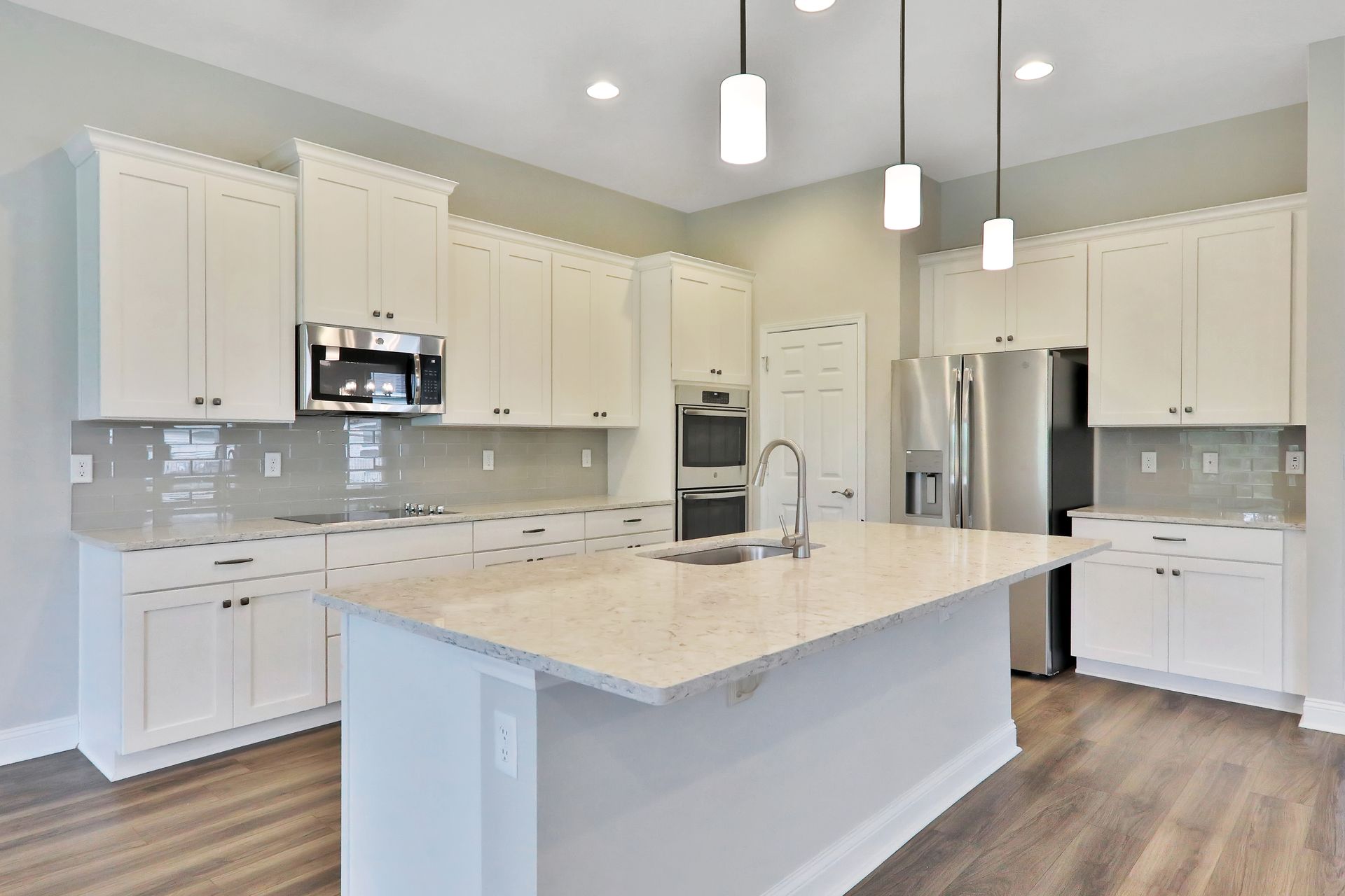 A kitchen with white cabinets , granite counter tops , stainless steel appliances and a large island.