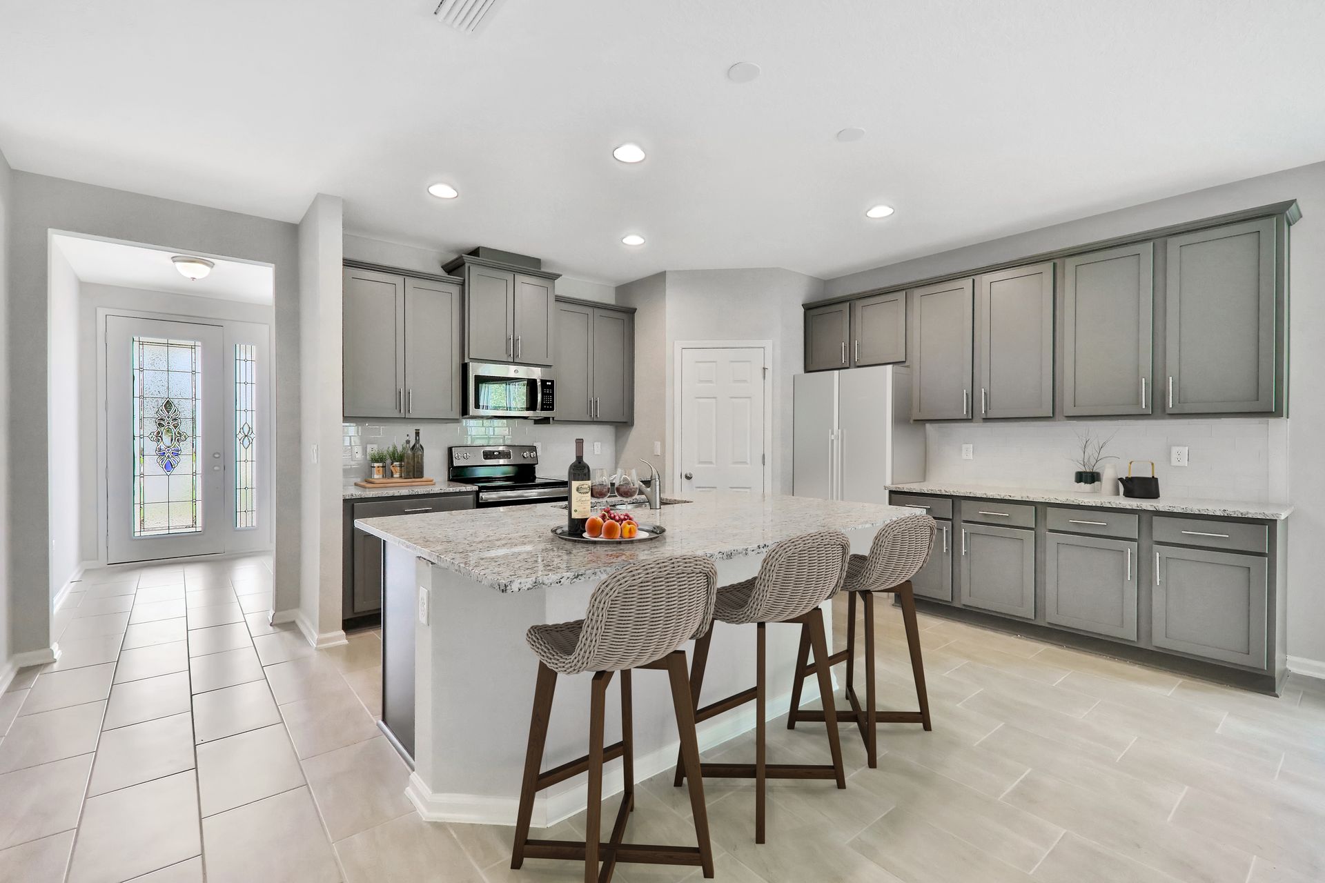 A kitchen with gray cabinets , white counter tops , a large island and stools.