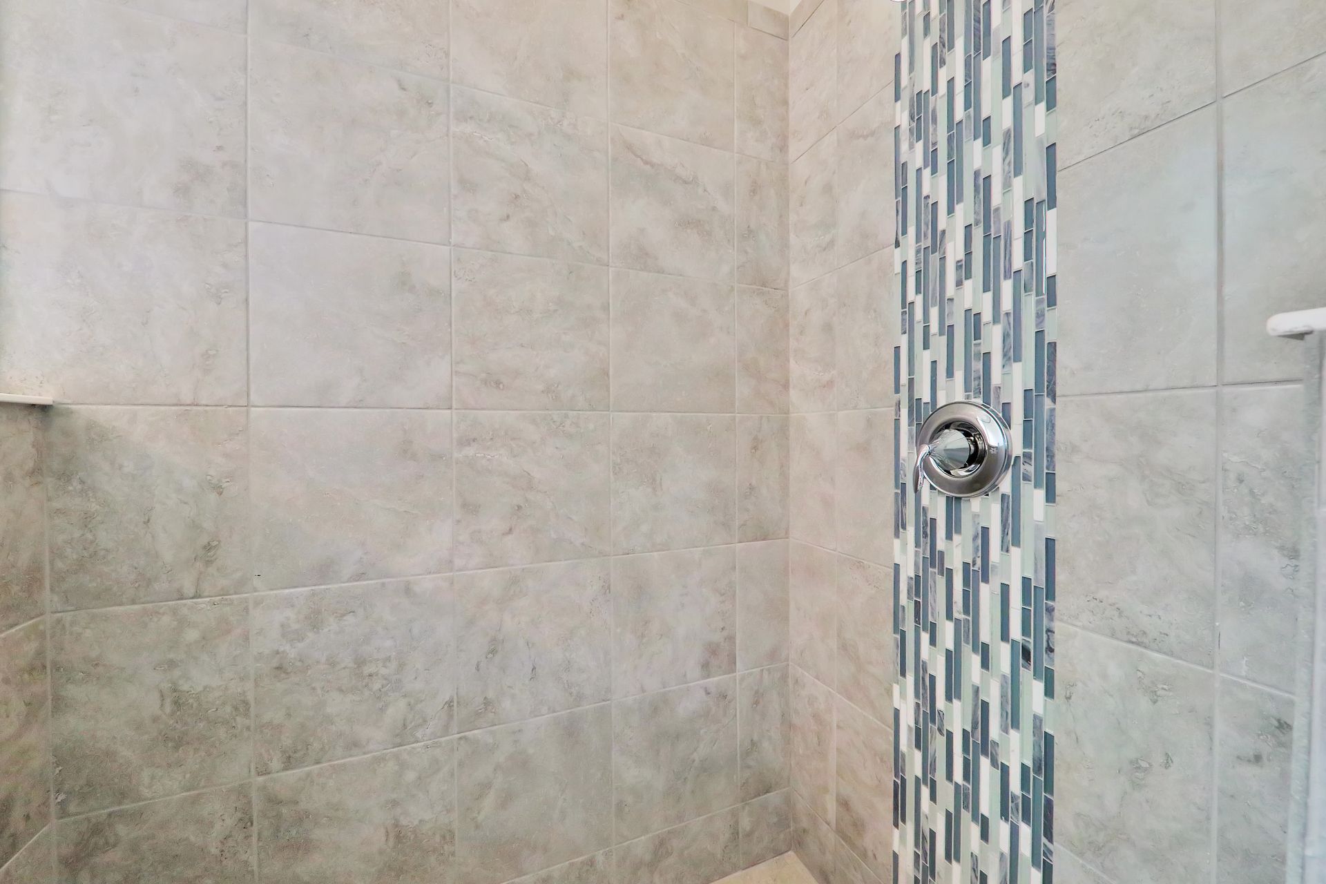 A bathroom with a walk in shower and a mosaic tile wall.