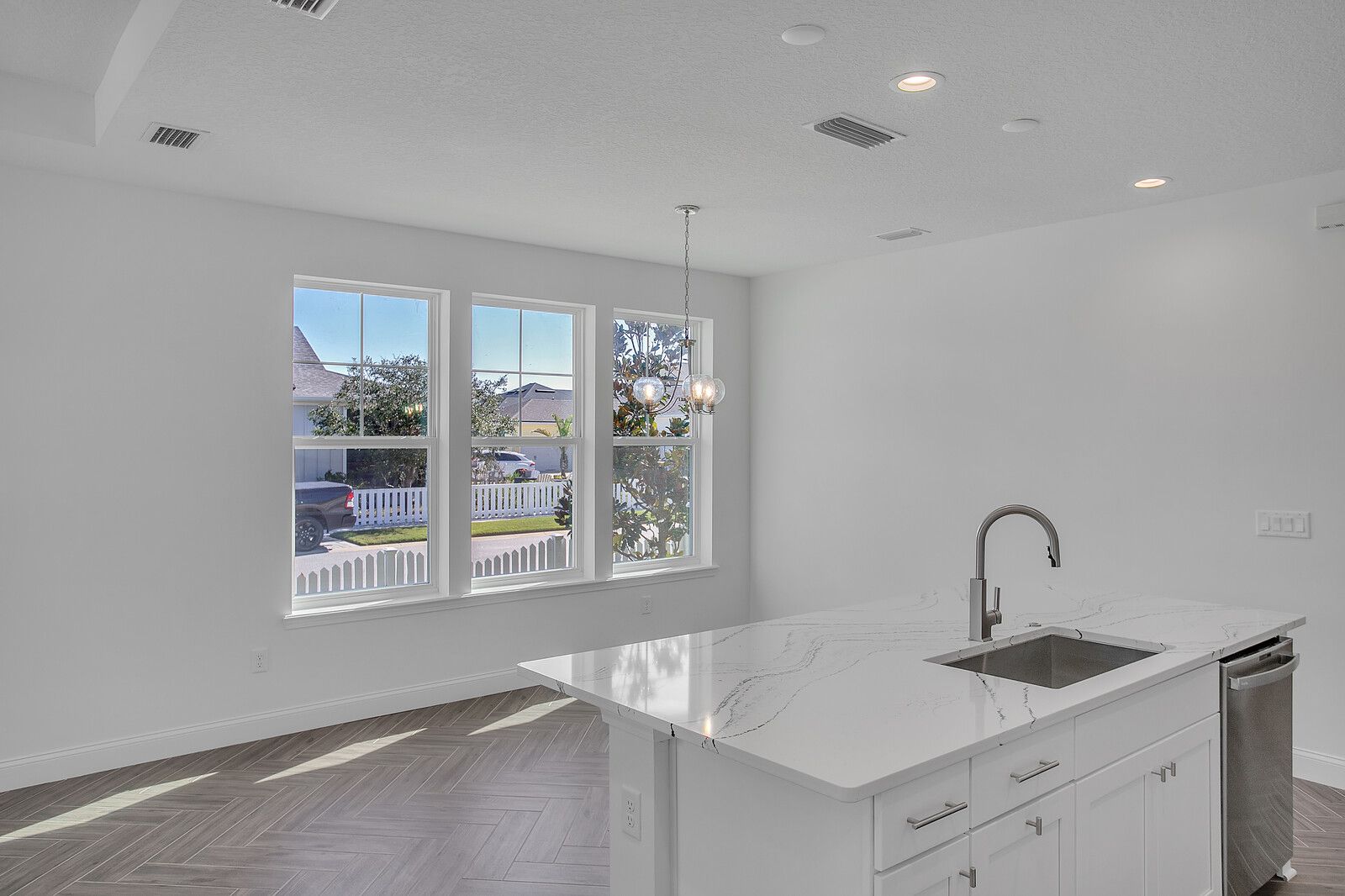 An empty kitchen with a sink , dishwasher , and large windows.