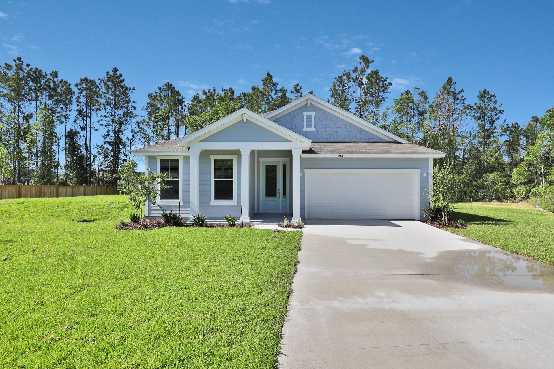 A white house with a garage and a driveway is sitting on top of a lush green field.
