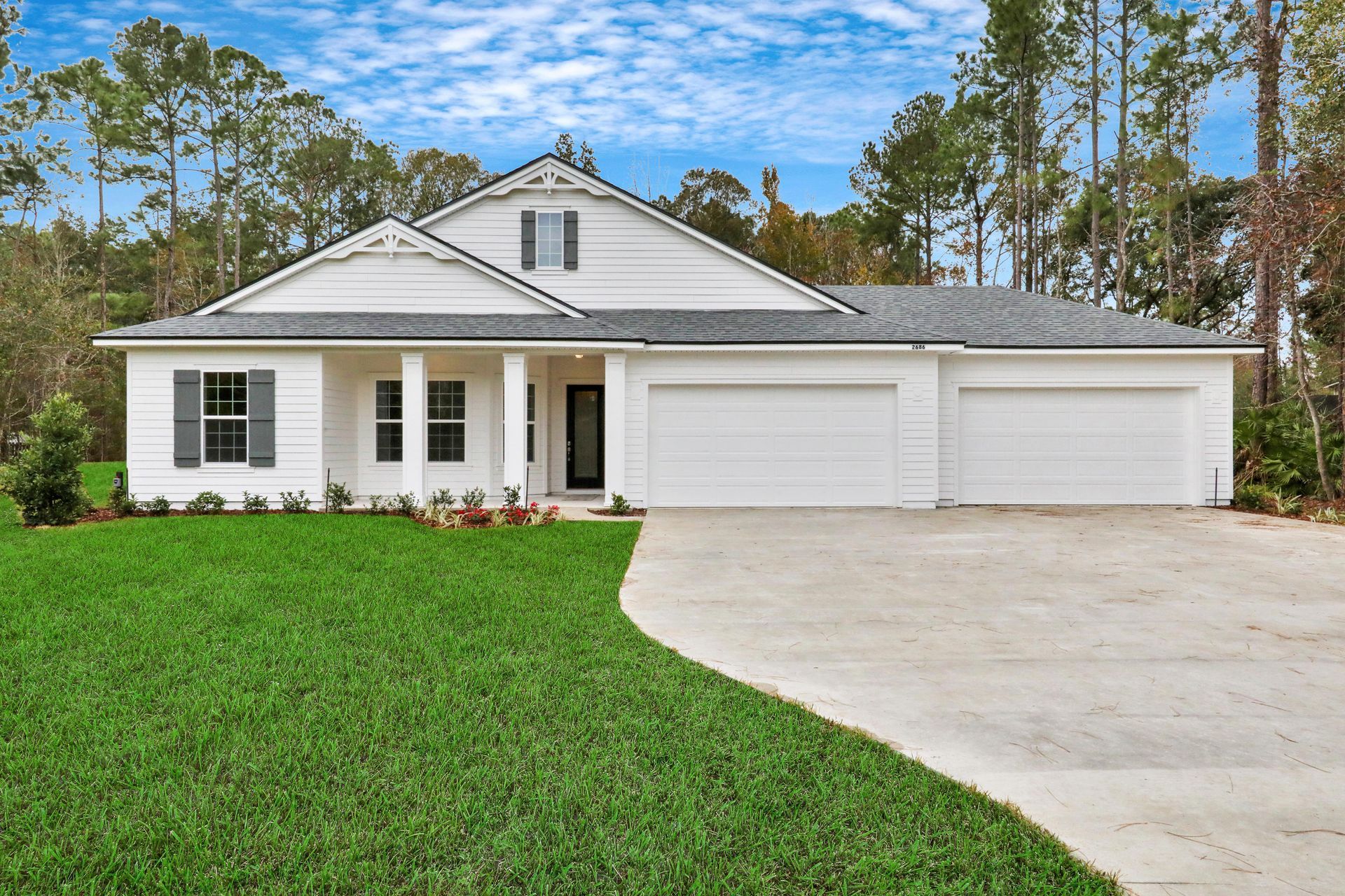A white house with a large driveway and a large lawn in front of it.