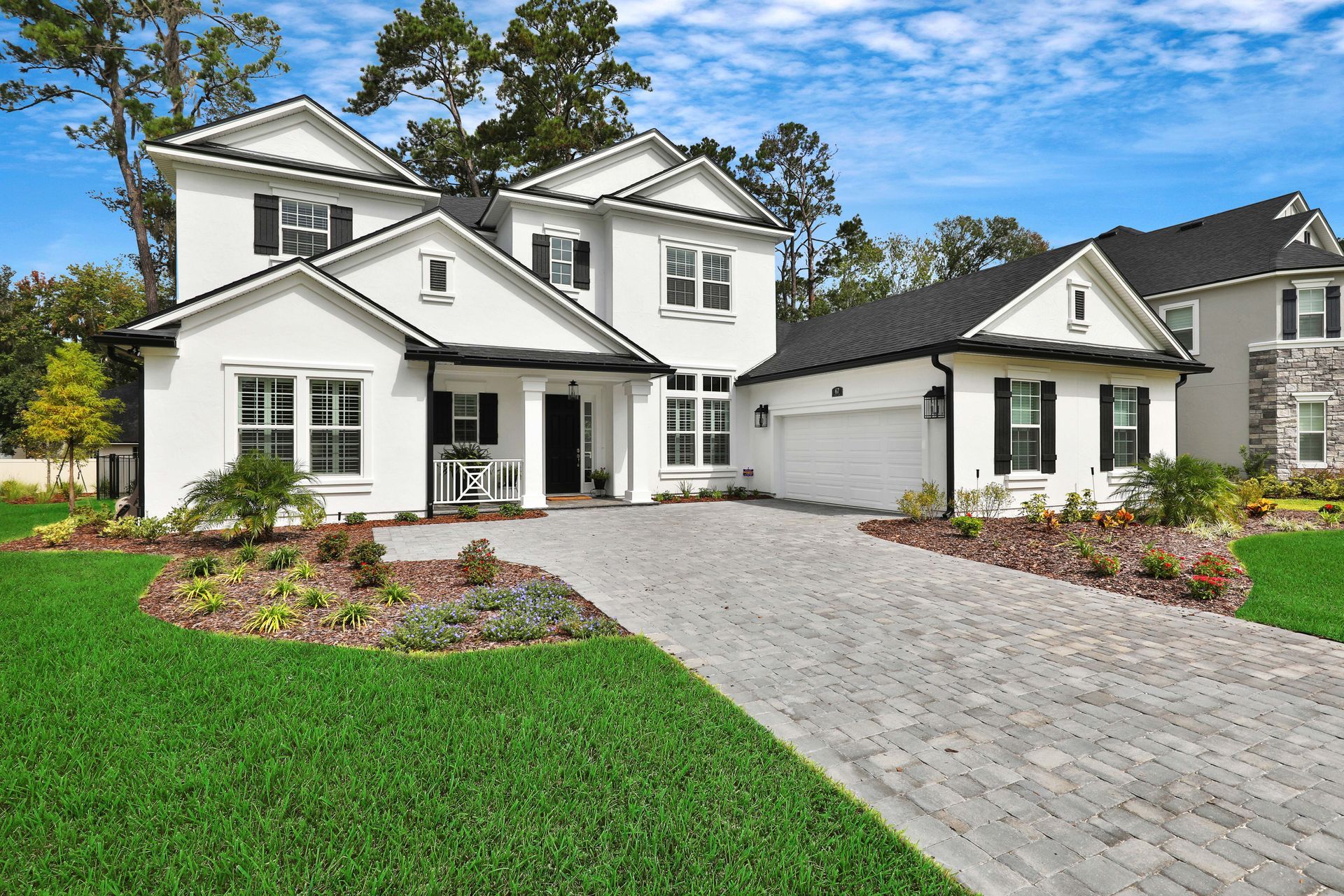 A large white house with a brick driveway and a large lawn in front of it.