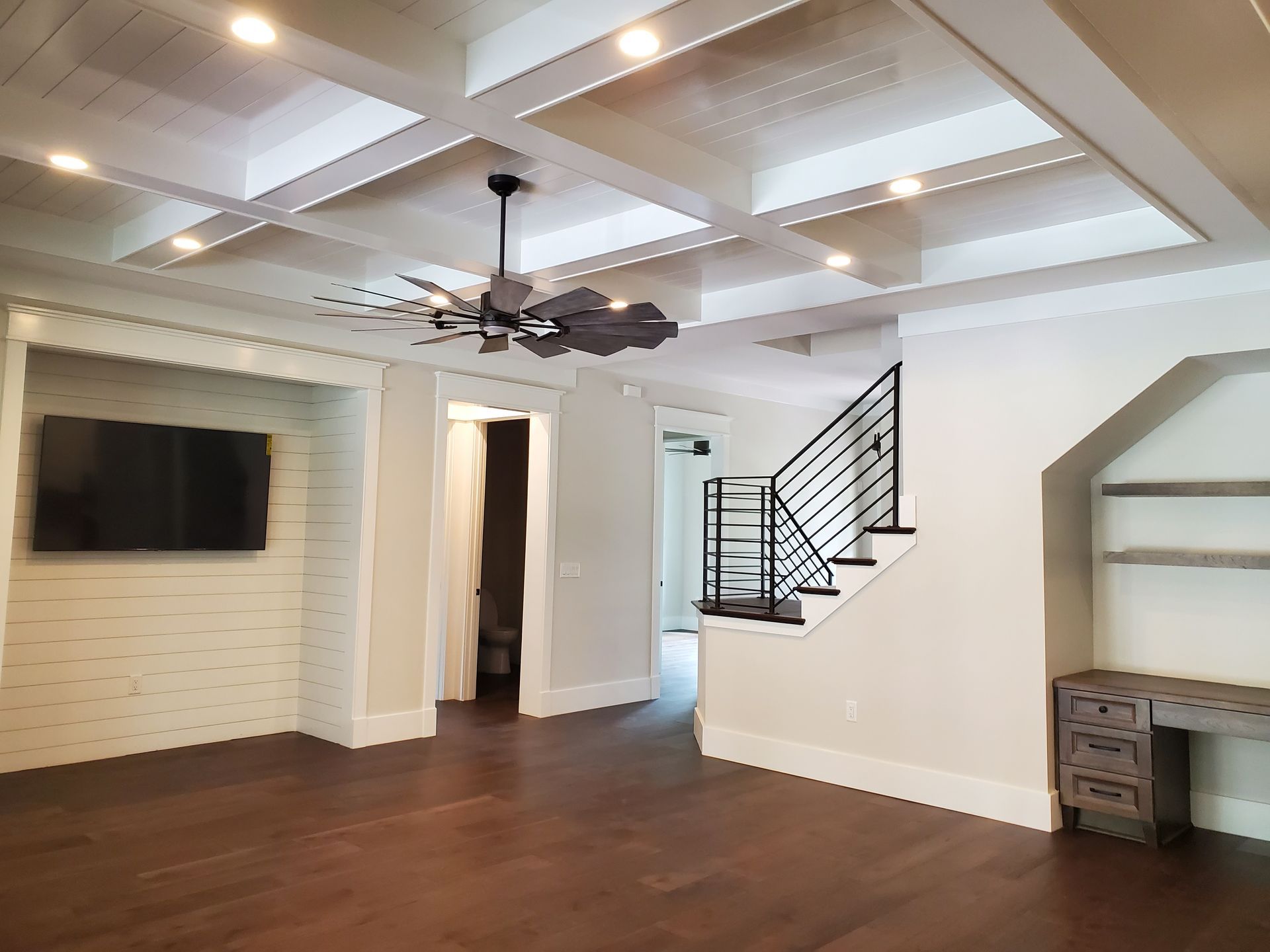An empty living room with a ceiling fan and stairs.