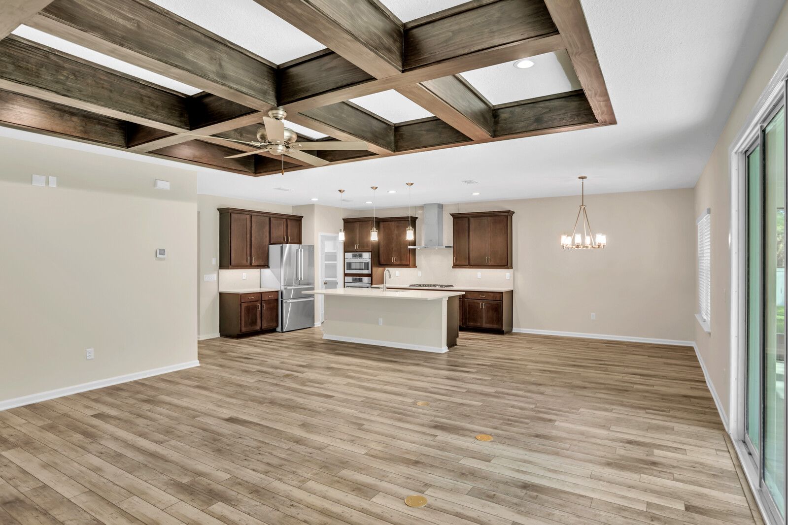 A large empty room with hardwood floors and a kitchen in the background.