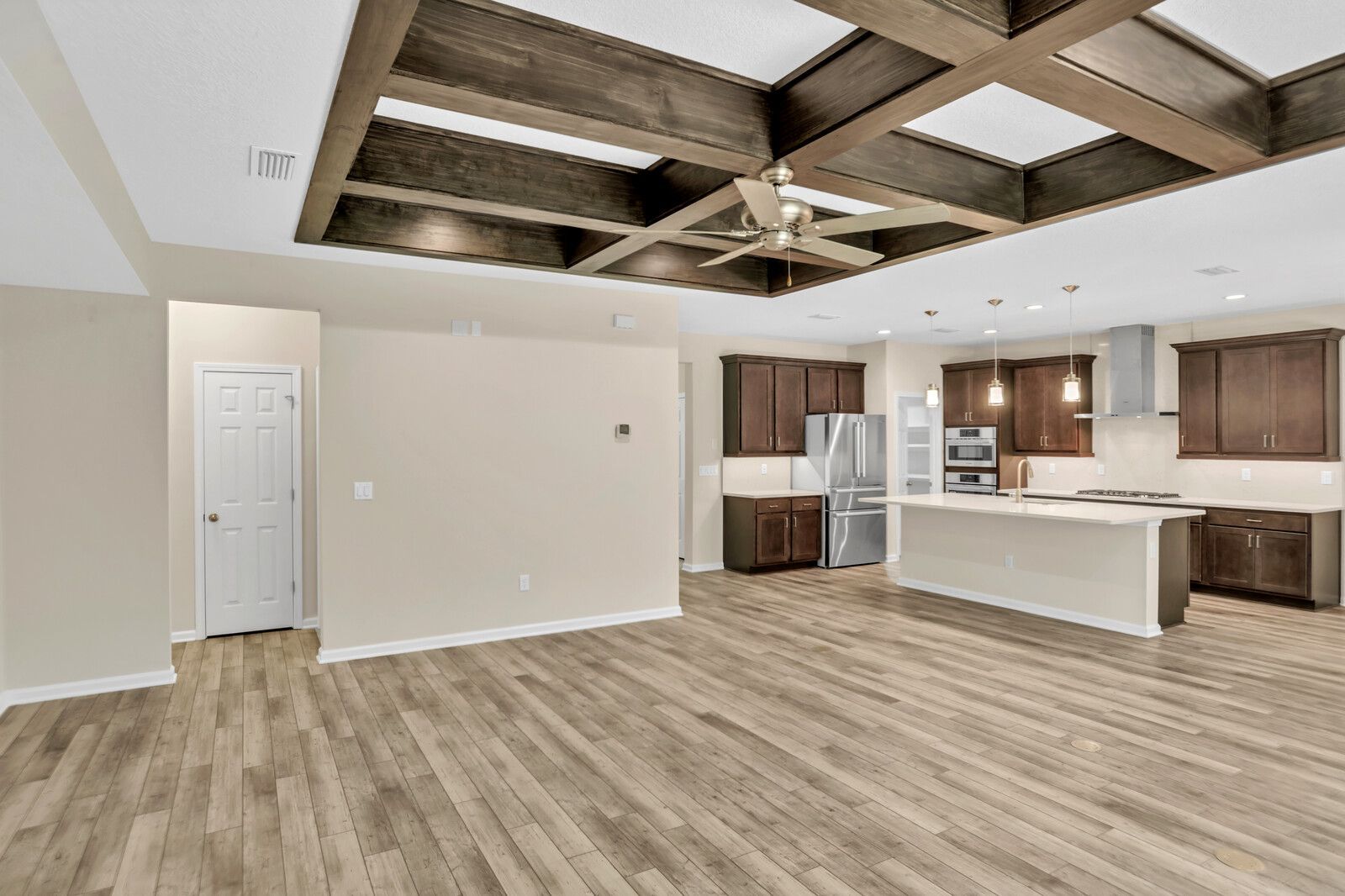 A large empty room with hardwood floors and a kitchen.