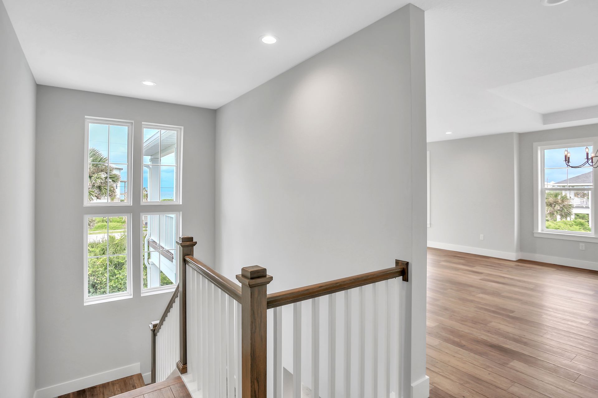 A staircase in an empty house with a wooden railing and lots of windows.