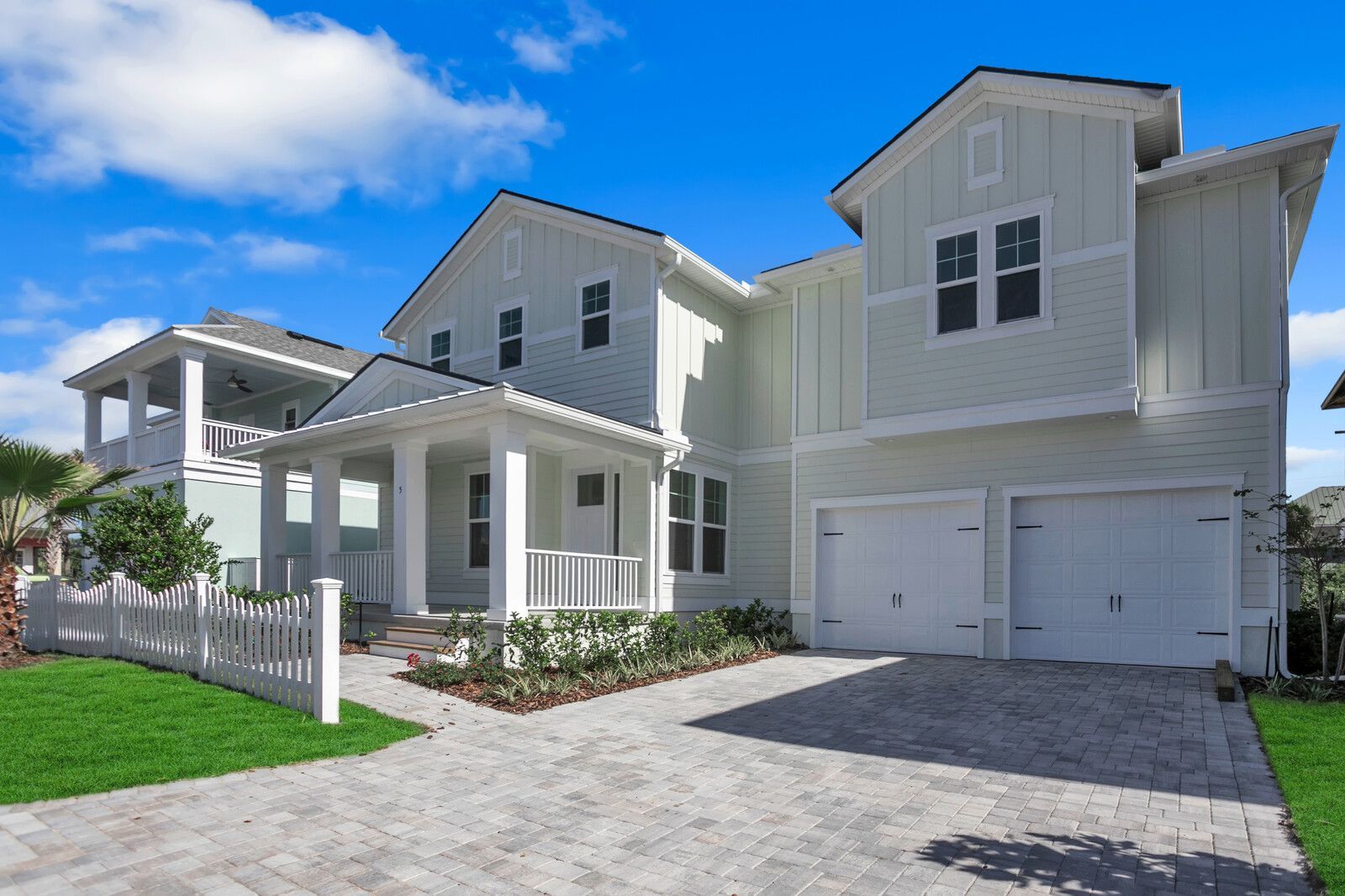 A large white house with two garages and a white picket fence