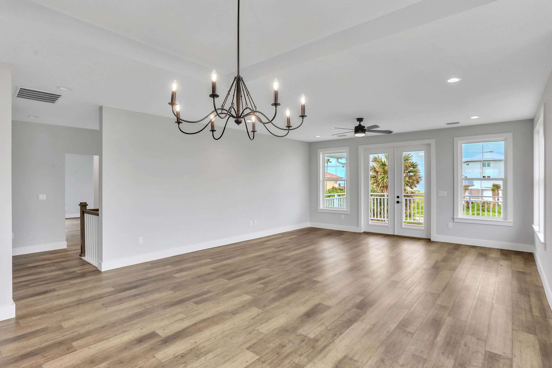 An empty living room with hardwood floors and a chandelier hanging from the ceiling.