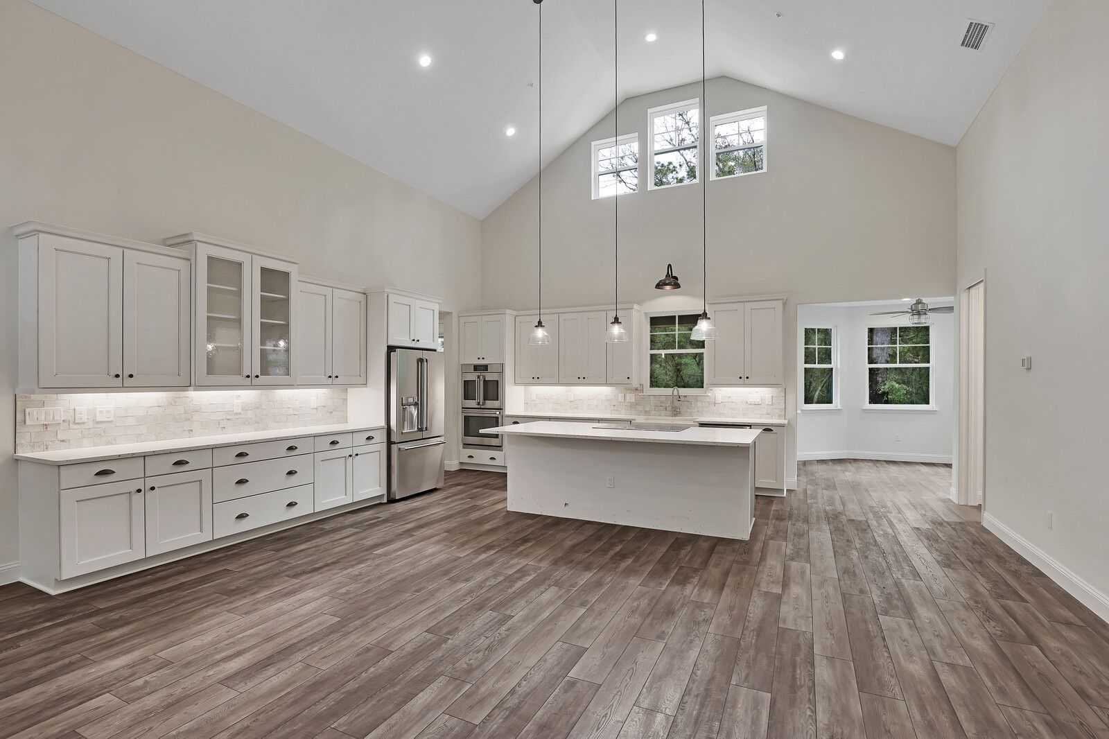 A large empty kitchen with white cabinets and hardwood floors.