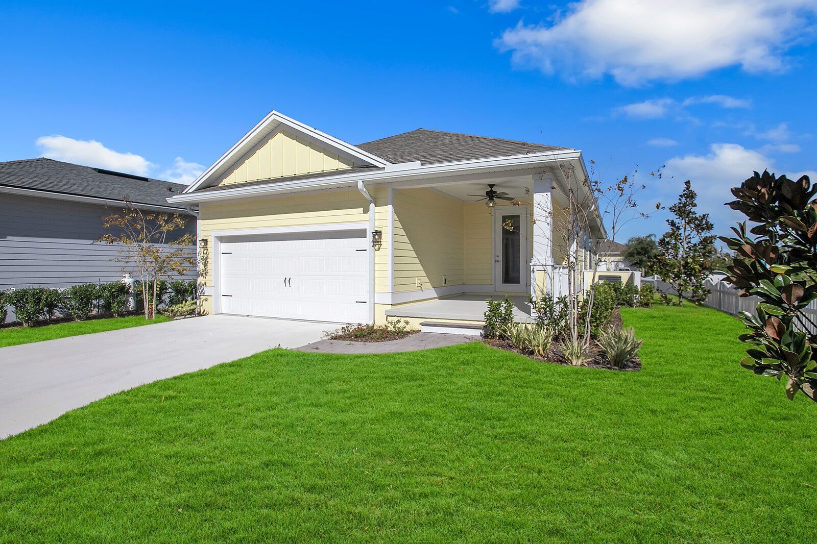 A yellow house with a white garage door and a lush green lawn.