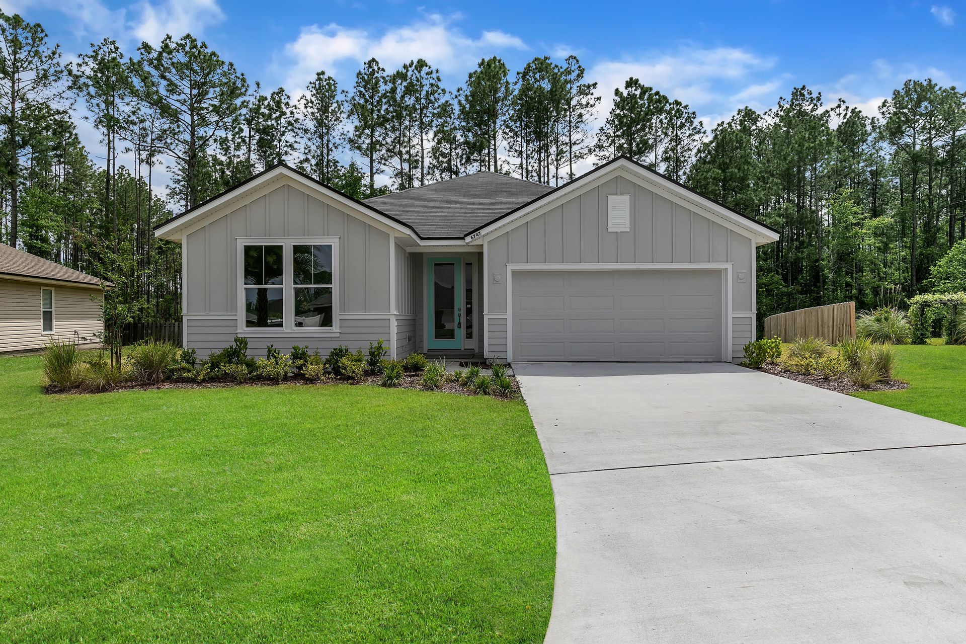 The front of a house with a concrete driveway and trees in the background.